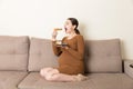 Hungry pregnant woman is eating pastry with great pleasure relaxing on the sofa at home. Happy pregnancy concept Royalty Free Stock Photo