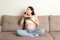 Hungry pregnant woman is eating a piece of tasty cake relaxing on the sofa at home. Sweet cravings during pregnancy Royalty Free Stock Photo