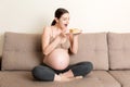 Hungry pregnant woman is eating a piece of tasty cake relaxing on the sofa at home. Sweet cravings during pregnancy Royalty Free Stock Photo