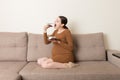 Hungry pregnant woman is eating a piece of tasty cake relaxing on the sofa at home. Sweet cravings during pregnancy Royalty Free Stock Photo