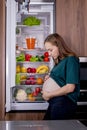 Hungry pregnant woman standing near refrigerator looking for food during pregnancy. Healthy eating Royalty Free Stock Photo