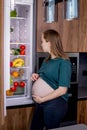 Hungry pregnant woman standing near refrigerator looking for food during pregnancy. Healthy eating Royalty Free Stock Photo