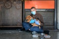 Hungry sick homeless beggar man on the street with his dog begging for money and food to eat wearing the medicine mask and gloves