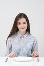 Hungry thin girl sitting at the table in front of an empty plate with a knife and fork.