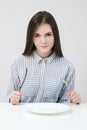 Hungry thin girl sitting at the table in front of an empty plate with a knife and fork. Royalty Free Stock Photo