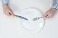 Hungry thin girl sitting at the table in front of an empty plate with a knife and fork. Royalty Free Stock Photo