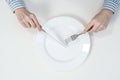 Hungry thin girl sitting at the table in front of an empty plate with a knife and fork.