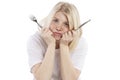 Hungry upset young woman with a fork and knife in her hands sitting at an empty table. Isolated over white background Royalty Free Stock Photo