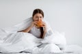 Hungry young female greedily eating burger on bed. Eating disorder, consolation with overeating and gluttony Royalty Free Stock Photo