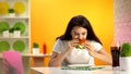 Hungry young lady eating tasty cheeseburger in cafe, soft drink glass on table