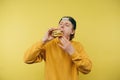 A hungry young man in a cap bites a burger with his eyes closed on a yellow background and keeps the pleasure of eating fast food