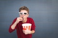 Hungry young man in 3D glasses eats popcorn from a cup and looks at the camera Royalty Free Stock Photo