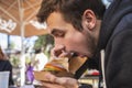 Hungry young man is sitting at the cafee terrace. He is looking at his burger, his mouth is wide open