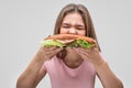 Hungry young woman bite burger. She devour it. Isolated on grey background.