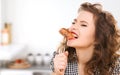 Hungry young woman eating meat on fork in kitchen