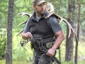 A hunter with a bow in the woods carries moose horns on his back and looking by side
