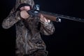 Hunter in camouflage clothing with a gun on a black background isolated. The man with the shotgun. Young guy in a camo suit with