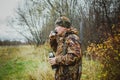 Hunter in camouflage clothing with a gun in a case drinking tea from a thermos