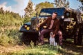 Hunter in elegant clothes holds a shotgun and sits together with his beagle dog while leaning against a retro military