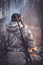 Hunter with gun at campfire in forest during hunting season. View from behind Royalty Free Stock Photo