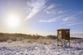 Hunter high seat in a snow covered winter landscape against a blue sky with a warm sun, copy space