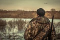 Hunter man hunting looking into the distance horizon in camouflage during hunting season rear view sunset river flood landscape Royalty Free Stock Photo