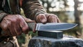 Hunter sharpens his hunting knife on whetstone under bright sunlight. Wilderness preparation concept Royalty Free Stock Photo