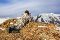 Hunter in winter camouflage in the mountains lying watching with binoculars