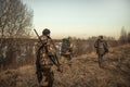 Hunting scene with group of hunters with hunting ammunition going through rural field during hunting season at sunset