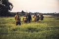 Hunting scene with group of men hunters going through tall grass on rural field at sunset during hunting season