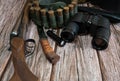 Hunting weapons, bandolier with cartridges, binoculars and a knife on a wooden background. Royalty Free Stock Photo