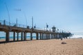 The Huntington Beach Pier as seen on a sunny day from a beach view looking up showing the concrete pillars on the underside of the