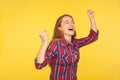 Hurray, triumph! Portrait of delighted happy girl in checkered shirt rejoicing victory with closed eyes and hands up, enjoying