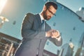 In a hurry. Young and handsome bearded businessman in eyeglasses and full suit checking the time while standing outdoors