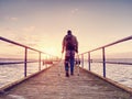 Hurt man with hooded jacket and forearm crutches standing on sea bridge Royalty Free Stock Photo