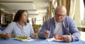 Husband bald and glasses and dark-haired middle-aged wife, sitting in a cafe, eat, communicate. In the hands of they