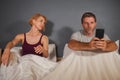 Husband or boyfriend using mobile phone in bed and suspicious frustrated wife or girlfriend feeling upset suspecting betrayal and