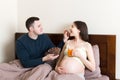 Husband is feeding his pregnant woman relaxing in bed with chocolate cereal balls and juice. Dry breakfast choco pops. Morning Royalty Free Stock Photo