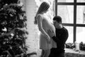 Husband kisses belly of his pregnant wife near Christmas tree. B