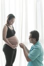 Husband measuring his pregnant wife`s belly with tape over white background