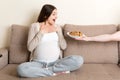 Husband offers his pregnant wife chocolate cookies relaxing on the sofa at home. Future father takes care about expecting mother