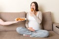 Husband offers his pregnant wife croissants relaxing on the sofa at home. Future father takes care about expecting mother