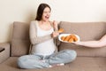 Husband offers his pregnant wife croissants relaxing on the sofa at home. Future father takes care about expecting mother