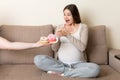 Husband offers his pregnant wife donuts relaxing on the sofa at home. Future father takes care about expecting mother