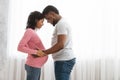 Husband and pregnant wife cuddling next to window at home