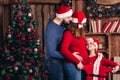 Husband, pregnant wife and daughter hold a Christmas costume for the baby.