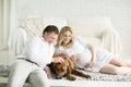 husband, pregnant wife and dog resting on the bed with the bedro