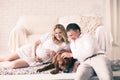 Husband, pregnant wife and dog resting on the bed with the bedro