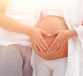 Husband and pregnant wife with folded hands in the shape of a heart on his tummy Royalty Free Stock Photo