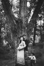 A husband, a pregnant wife and a little son are standing near a big tree, the child is holding a dad by his pants